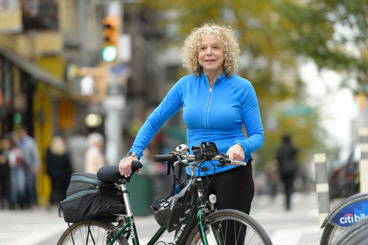 MSK patient outside in the streets of New York City holding a bike and smiling at the camera.