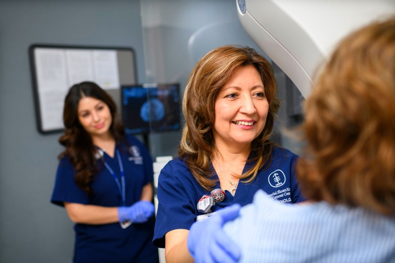 Two female healthcare professionals performing a mammogram on a patient