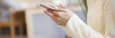 A woman's torso, arms, and hands are shown. She is holding a smart phone.